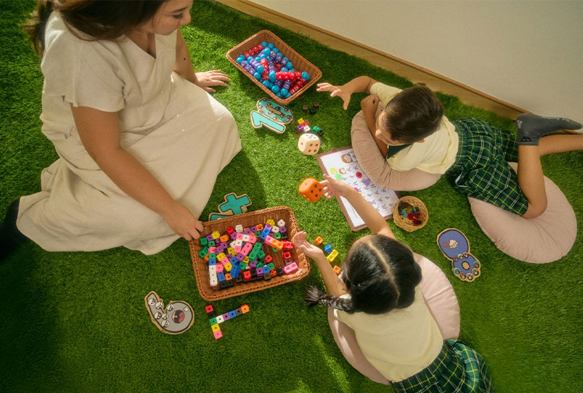 Children and a teacher playing with building blocks on a grass mat